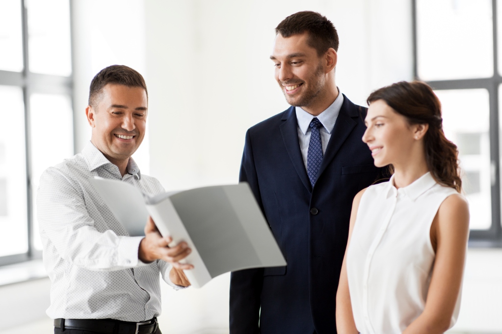 Real estate business, sale and people concept - happy smiling realtor with folder showing documents to customers at new office room